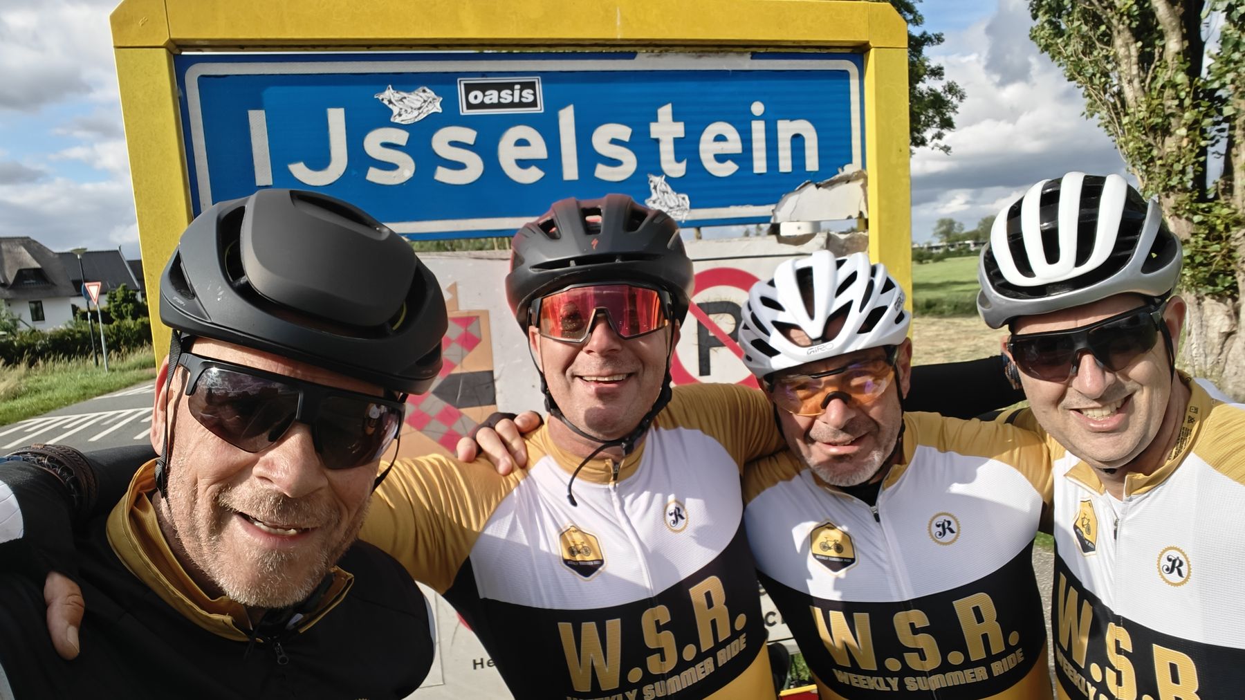Vier WSR-rijders in clubshirts, arm in arm voor het plaatsnaambord van IJsselstein